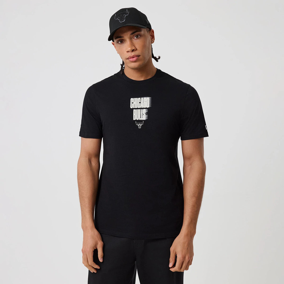 New Era Chicago Bulls NBA Graphic Black T-Shirt, front view on a model showing the Chicago Bulls lettering with the team logo printed below, and the embroidered New Era logo on the left sleeve, paired with black trousers.