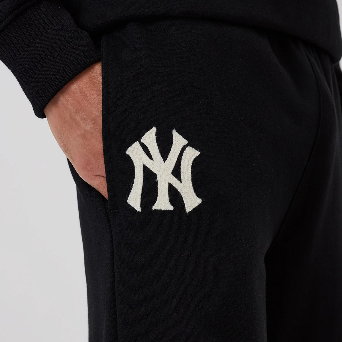 New Era New York Yankees MLB Black Wide Leg Joggers, close-up showing the raised white Yankee logo embroidered on the left thigh, with hands casually placed in the side pocket, highlighting the adjustable waistband.