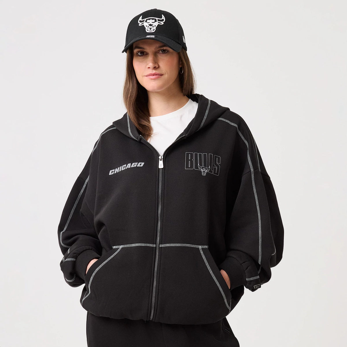 New Era Chicago Bulls NBA Graphic Black Pullover Hoodie, front view on a model, showcasing the white Chicago lettering on the upper right, a Bulls logo beneath chest graphics on the left, and prominent white stitching along the seams and pockets.