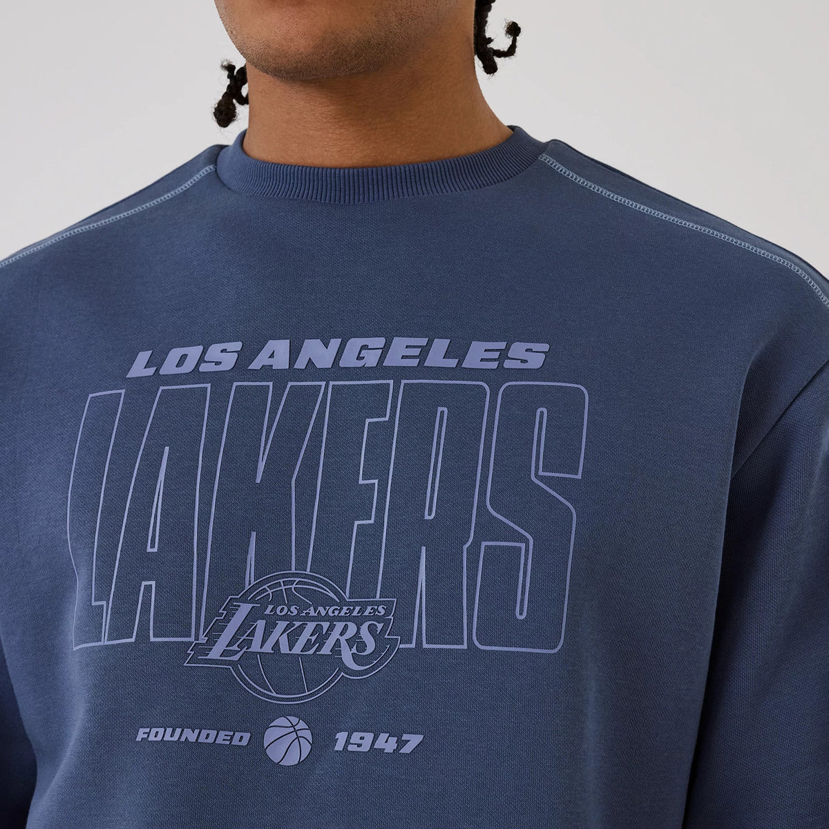New Era LA Lakers NBA Graphic Dark Blue Crew Neck Sweater, on-model view showing the printed Los Angeles Lakers text across the chest, a basketball emblem below, and small that reads Founded 1947 near the hem.
