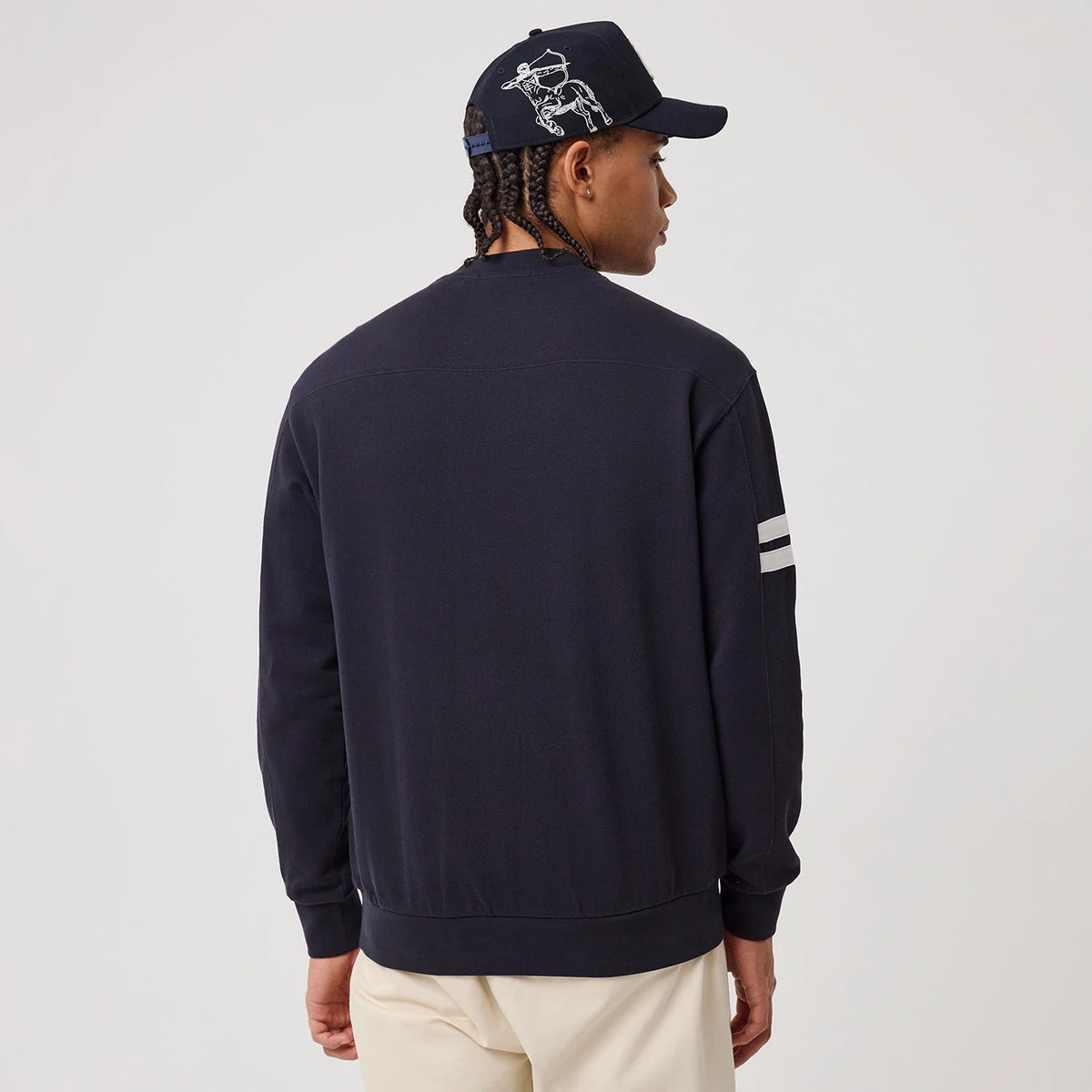 New Era New York Yankees MLB Arch Graphic Navy Crew Neck Sweater, back view on a model wearing a navy cap, showing the plain navy back of the sweater with two white stripes on the sleeve and a relaxed fit.