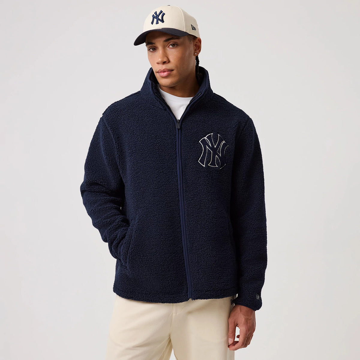 New Era New York Yankees MLB Dark Blue Sherpa Jacket, front view on a model showing the full zip closure and a large embroidered New York Yankees logo on the left chest, styled with a matching dark blue and white New York Yankees cap.