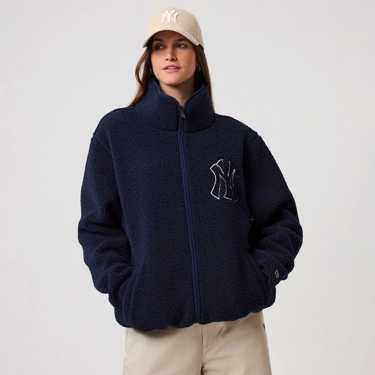 New Era New York Yankees MLB Dark Blue Sherpa Jacket, front view on a model wearing a cream cap, showing the full-length zip closure, a large embroidered New York Yankees logo on the chest, and a high collar for added style.