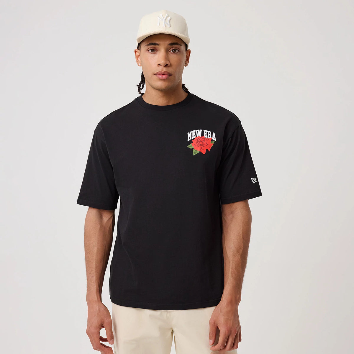 New Era Floral Graphic Black T-Shirt, front view on a model wearing a beige cap, featuring a large embroidered New Era logo with a red rose on the left chest and a small embroidered New Era flag logo on the left sleeve.