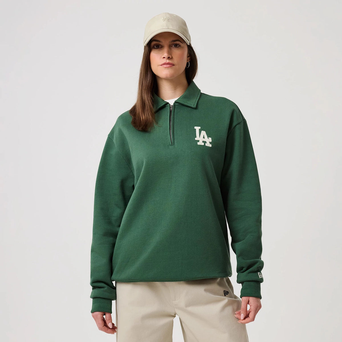 New Era LA Dodgers MLB Dark Green 1/4 Zip Sweater, front view on a model wearing a matching cap, features a white embroidered LA logo on the left chest, a ribbed collar with zip closure and the New Era flag logo on the left cuff.