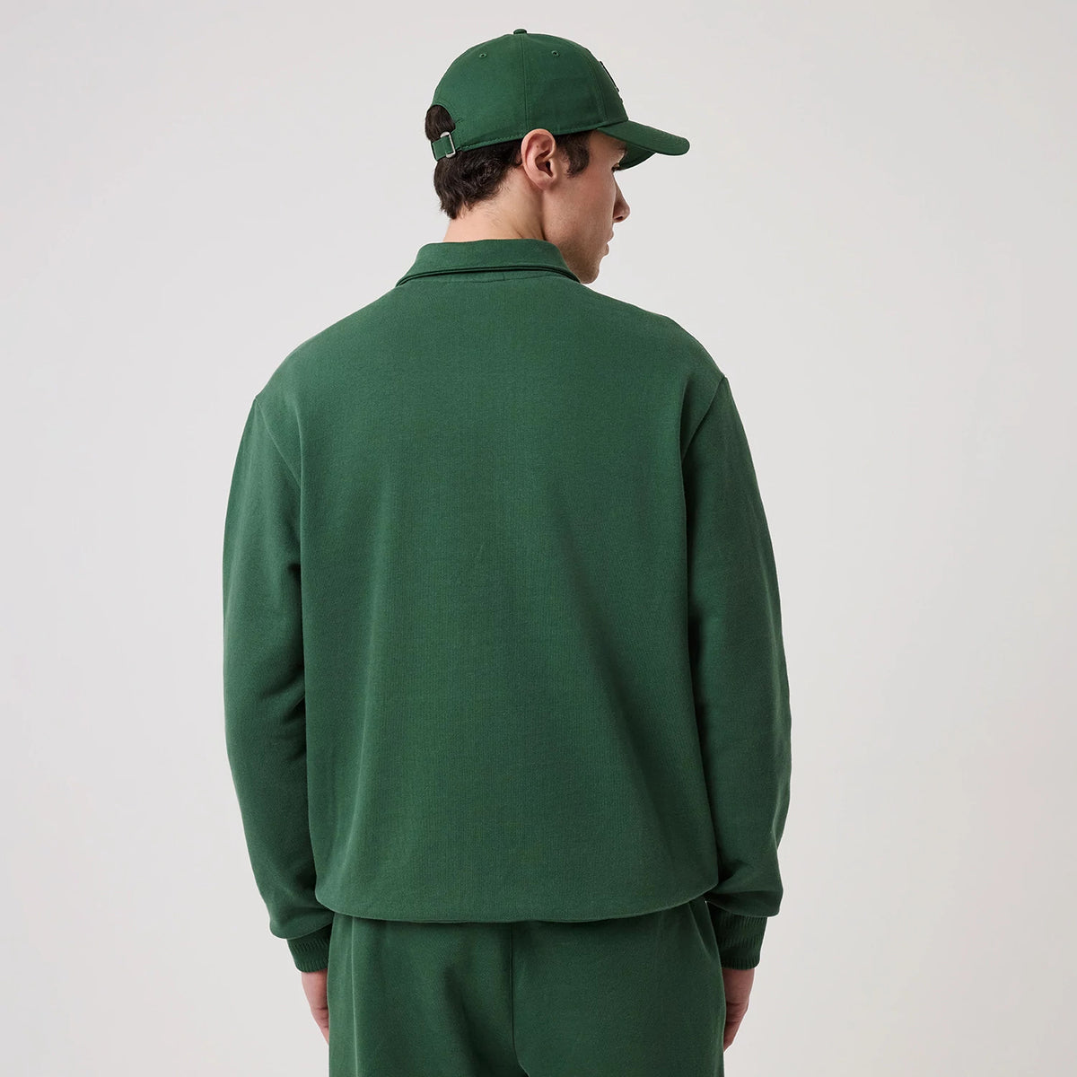 New Era LA Dodgers MLB Dark Green 1/4 Zip Sweater, back view on a model wearing a matching dark green cap, showing the sweater's plain back, straight hem, and ribbed cuffs, creating a cohesive look with the green outfit.