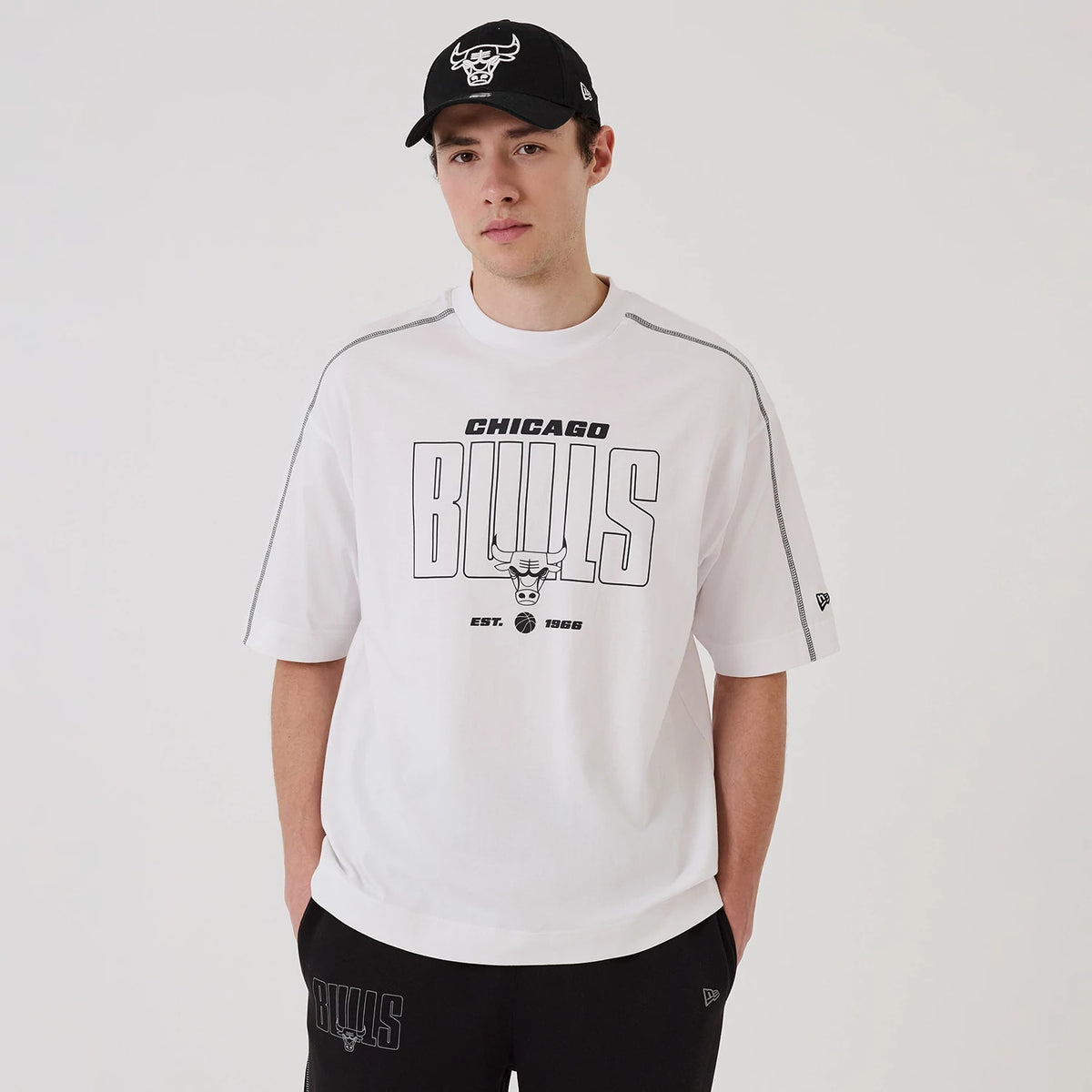 New Era Chicago Bulls NBA Graphic White Boxy T-Shirt, front view on-model showcasing the 'Chicago Bulls' graphic across the chest in black, an embroidered New Era logo on the left sleeve, and black side piping detail along the shoulders.