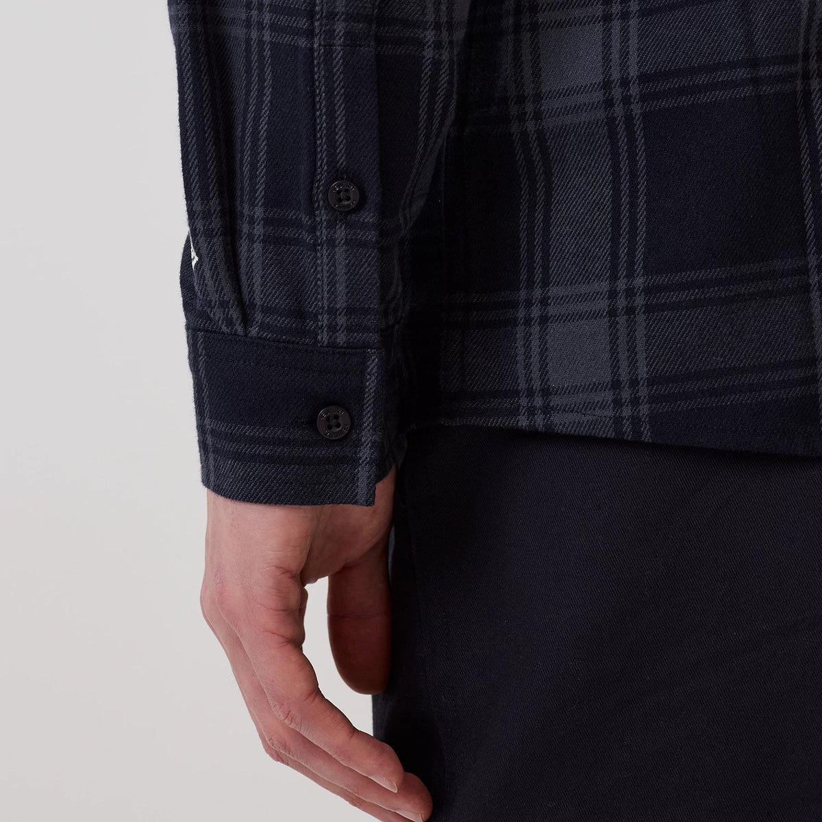 New Era New York Yankees MLB Plaid Navy Long Sleeve Shirt, close-up view featuring navy and grey plaid pattern, black buttons on the cuff, and a New Era flag logo on the left sleeve, worn with dark trousers.