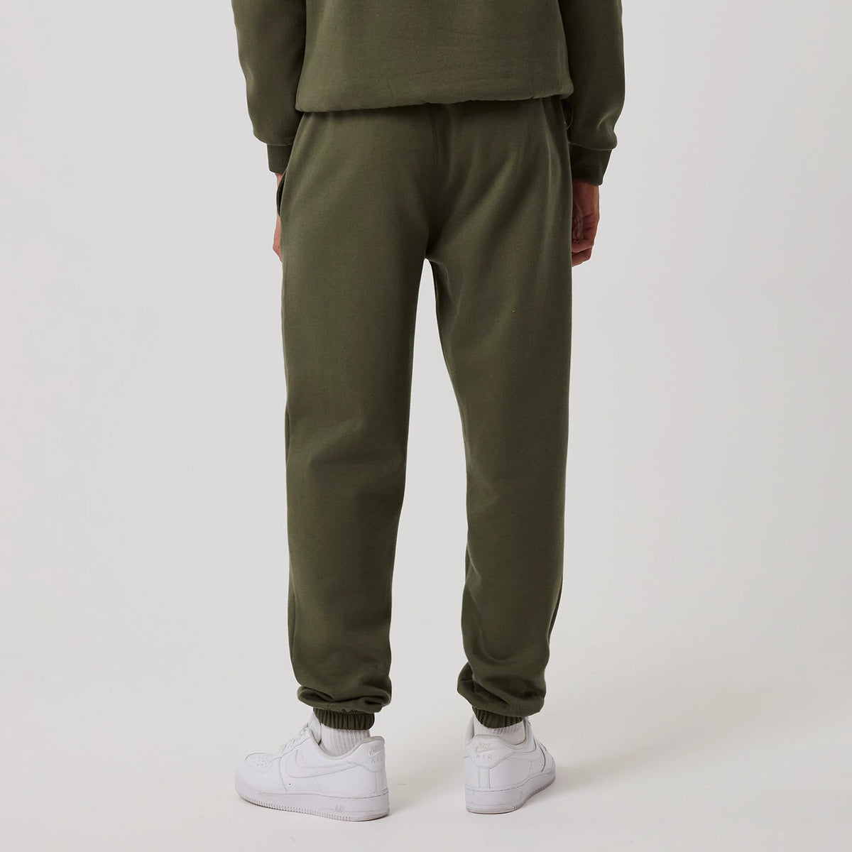 New Era New York Yankees MLB League Essential Green Joggers, rear view on a model showcasing the plain olive-green design with a cinched waistband and elasticated cuffs, paired with white trainers for a casual look.