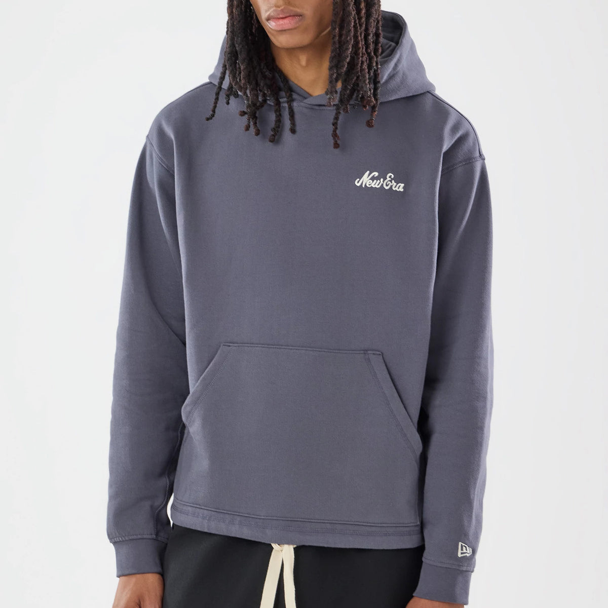 New Era Open Hem Grey Pullover Hoodie, front view on a model highlighting the grey colour and relaxed fit, featuring an embroidered New Era logo on the left chest, a drawstring hood, and a kangaroo pocket above black trousers.