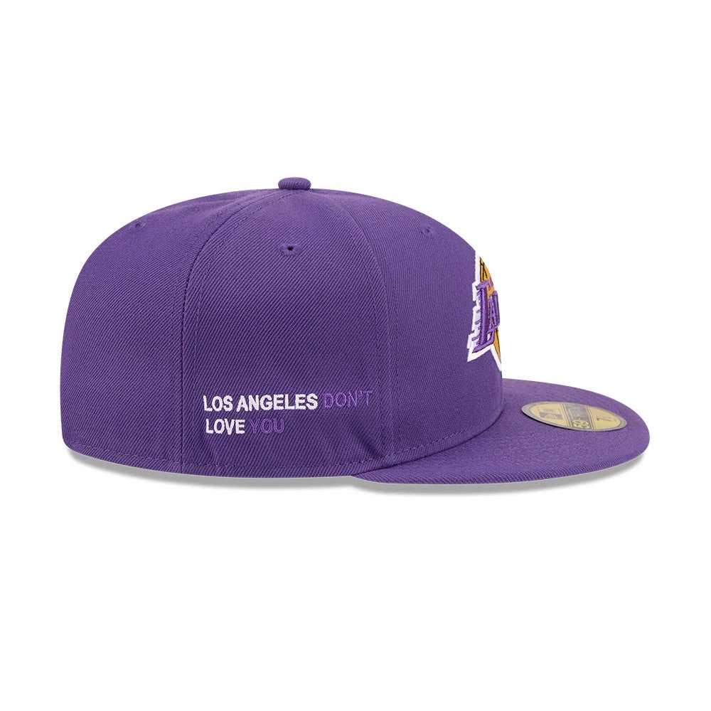 LA Lakers NBA X J-FROST Purple New Era 59FIFTY Fitted Cap, side view showing the embroidered message Los Angeles Don't Love You on the side panel, the structured purple crown, and the gold 59FIFTY size sticker on the flat purple visor.