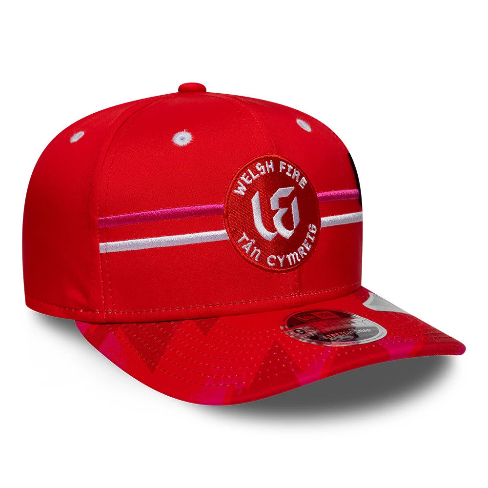 Welsh Fire Tan Cymreig The Hundred 2026 Red New Era 9SEVENTY Stretch Snap Adjustable Cap, front view showing a red and white circular logo with Welsh Fire lettering and stripes across the front panel, with a 9SEVENTY size sticker on the curved visor.