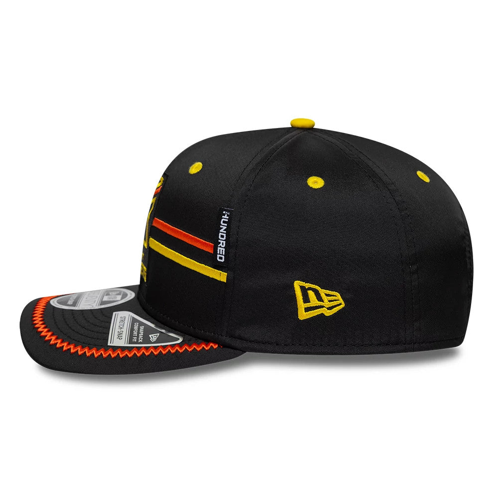 Trent Rockets The Hundred 2026 Black New Era 9SEVENTY Stretch Snap Adjustable Cap, side view showing black crown with yellow New Era flag logo on left side, yellow and orange stripes across the side panel, and yellow top button.