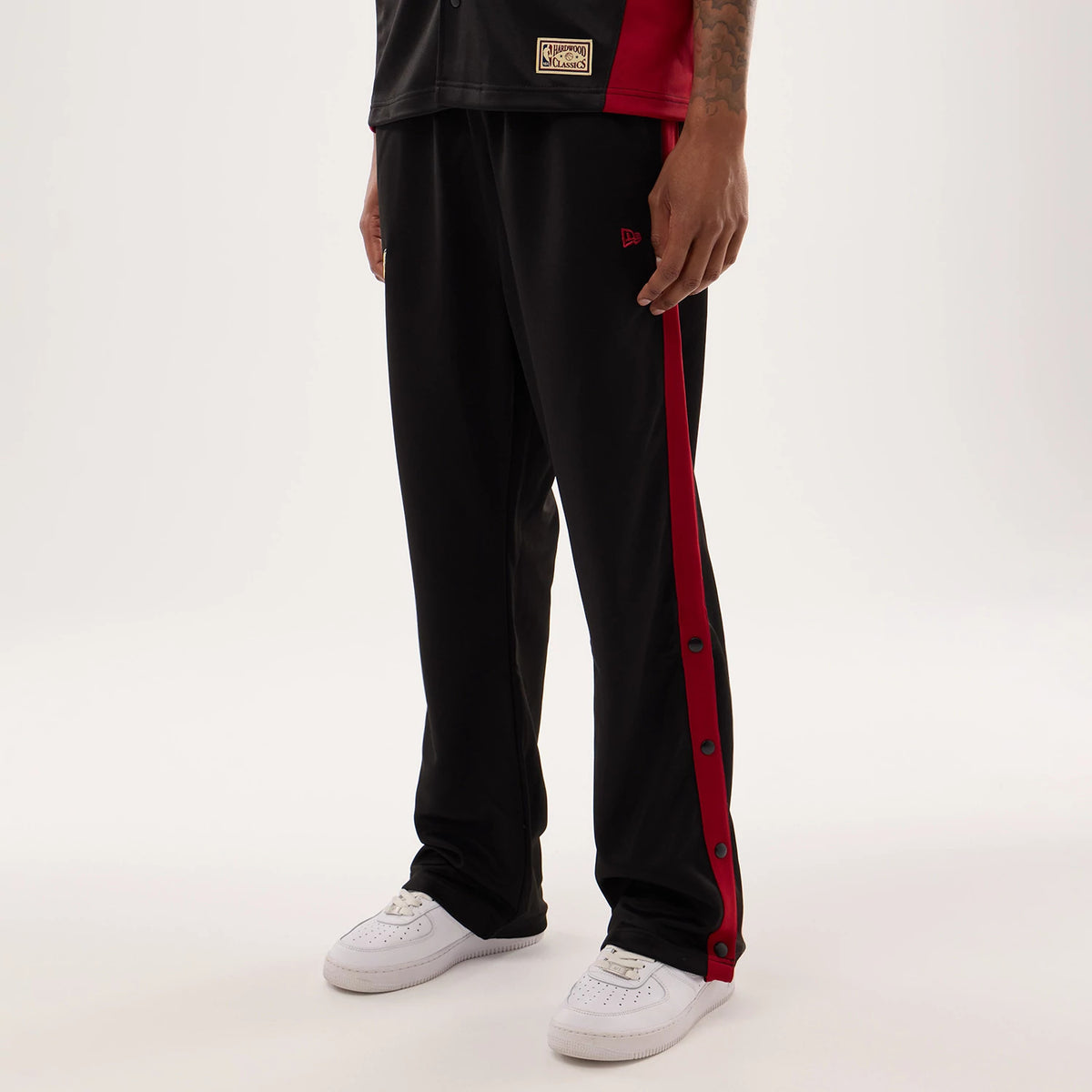 New Era Miami Heat NBA Hardwood Classic Straight Black Straight Leg Joggers, on-model view with black fabric and red side stripe featuring buttons, embroidered red New Era flag logo on the upper leg, paired with white trainers.