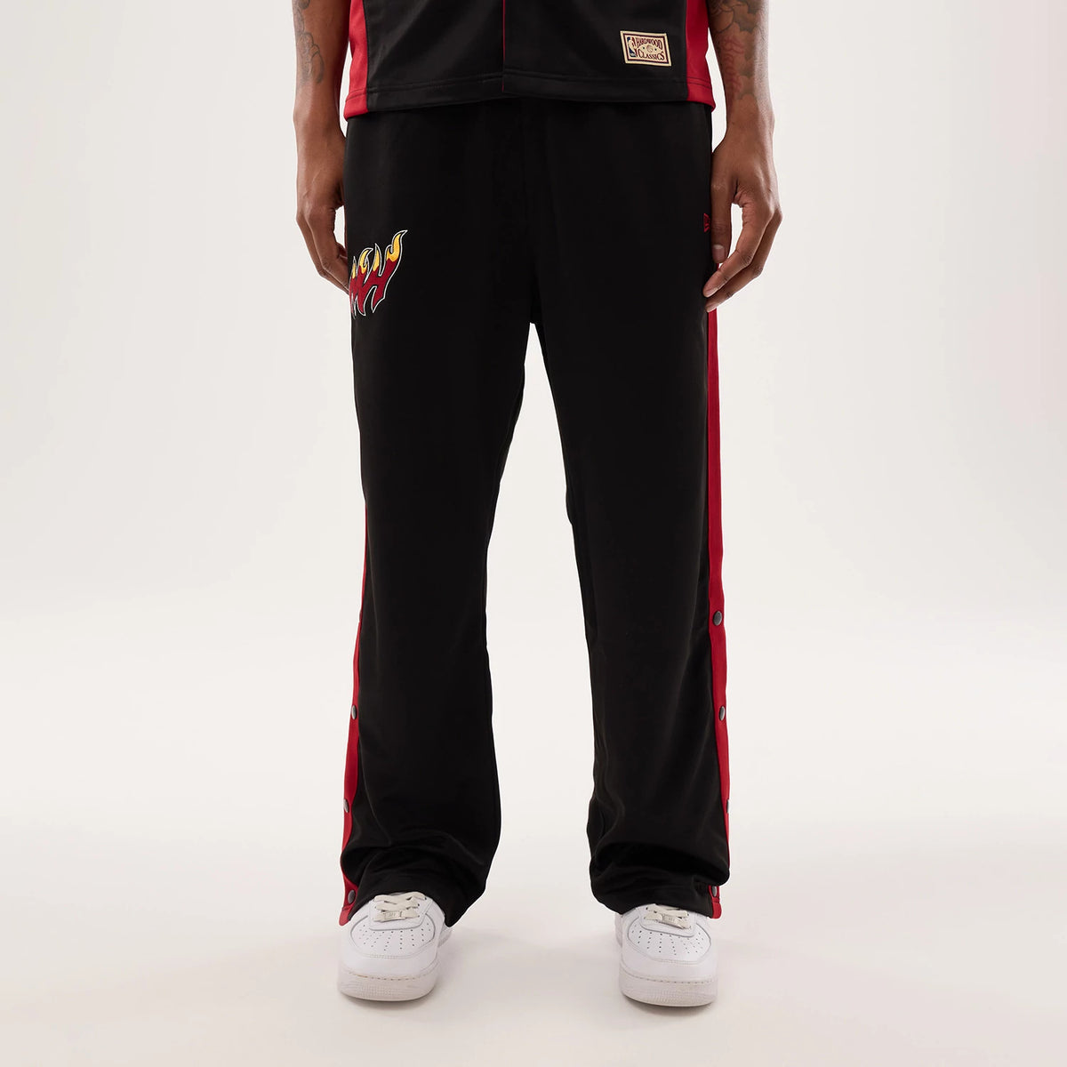 New Era Miami Heat NBA Hardwood Classic Straight Black Straight Leg Joggers, front view on a model showing the team’s flaming basketball logo embroidered on the right thigh, red side panels with snap buttons, and elasticated waistband.