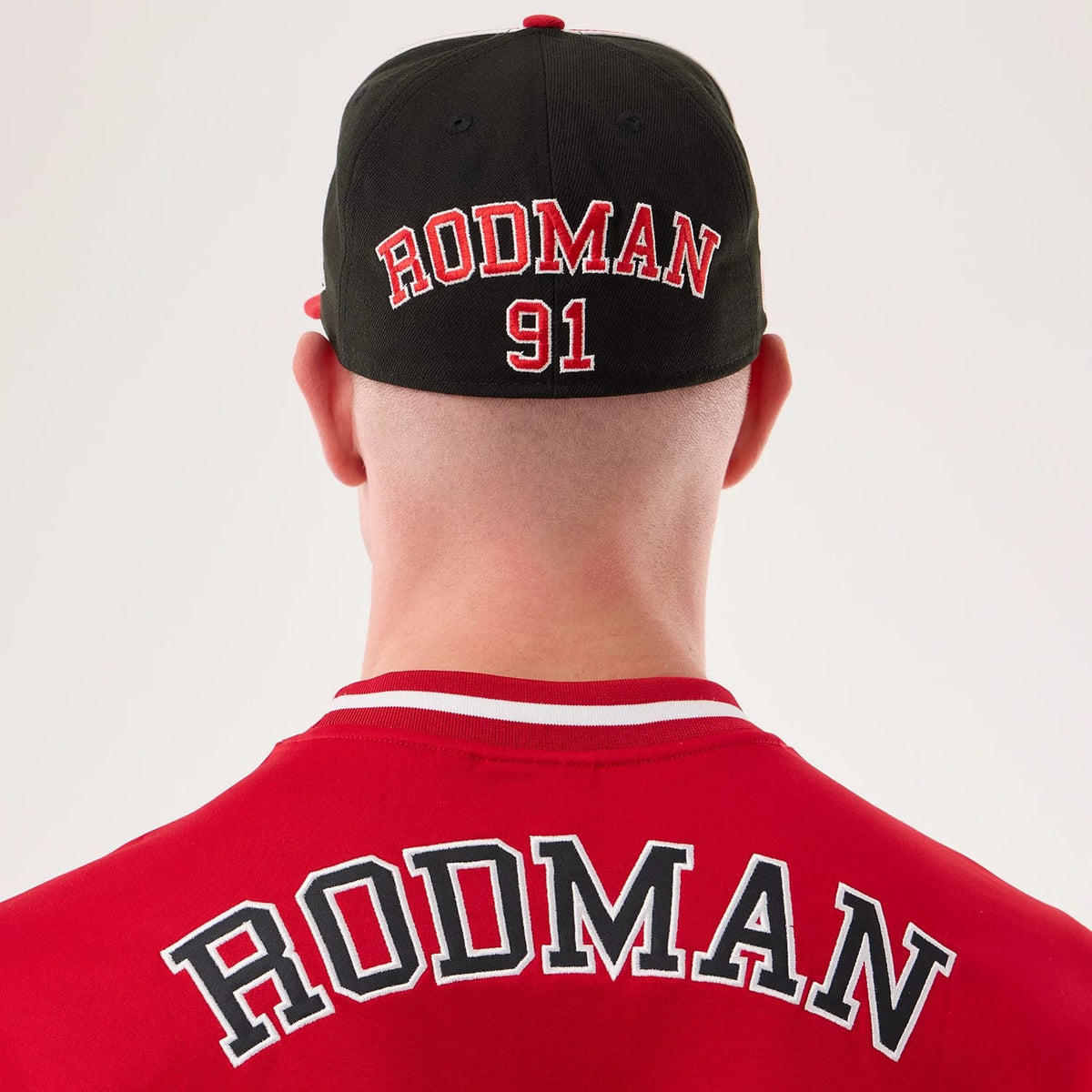 New Era Chicago Bulls NBA Hardwood Classic Mesh Oversized Red T-Shirt, back view on a model with a black cap showing embroidered Rodman lettering and the number 91 across the upper shoulders, with a ribbed collar featuring white and red stripes.