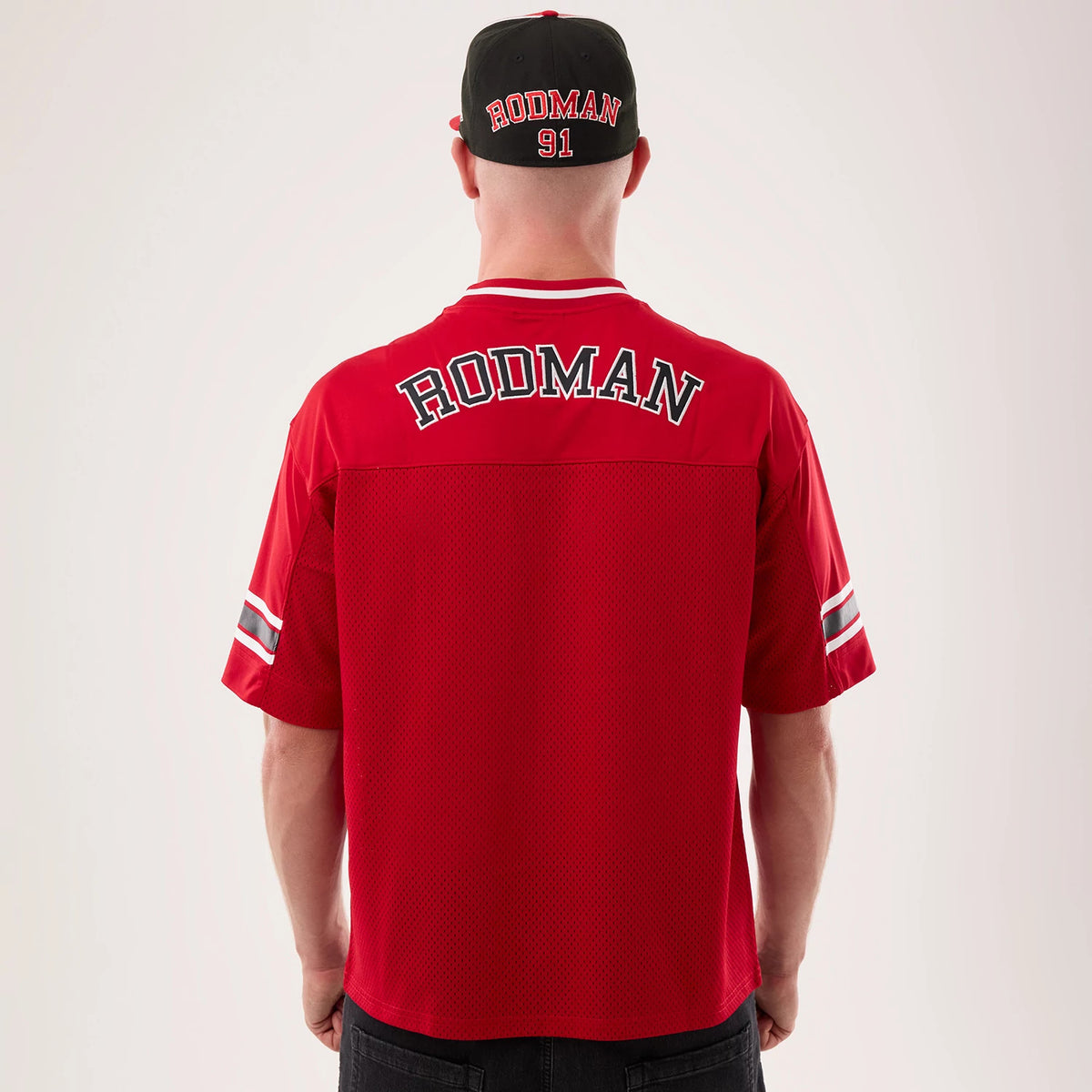 New Era Chicago Bulls NBA Hardwood Classic Mesh Oversized Red T-Shirt, back view on a model with a matching cap, featuring Rodman lettering across the shoulders, a mesh texture, and stripes on the sleeves for a classic look.