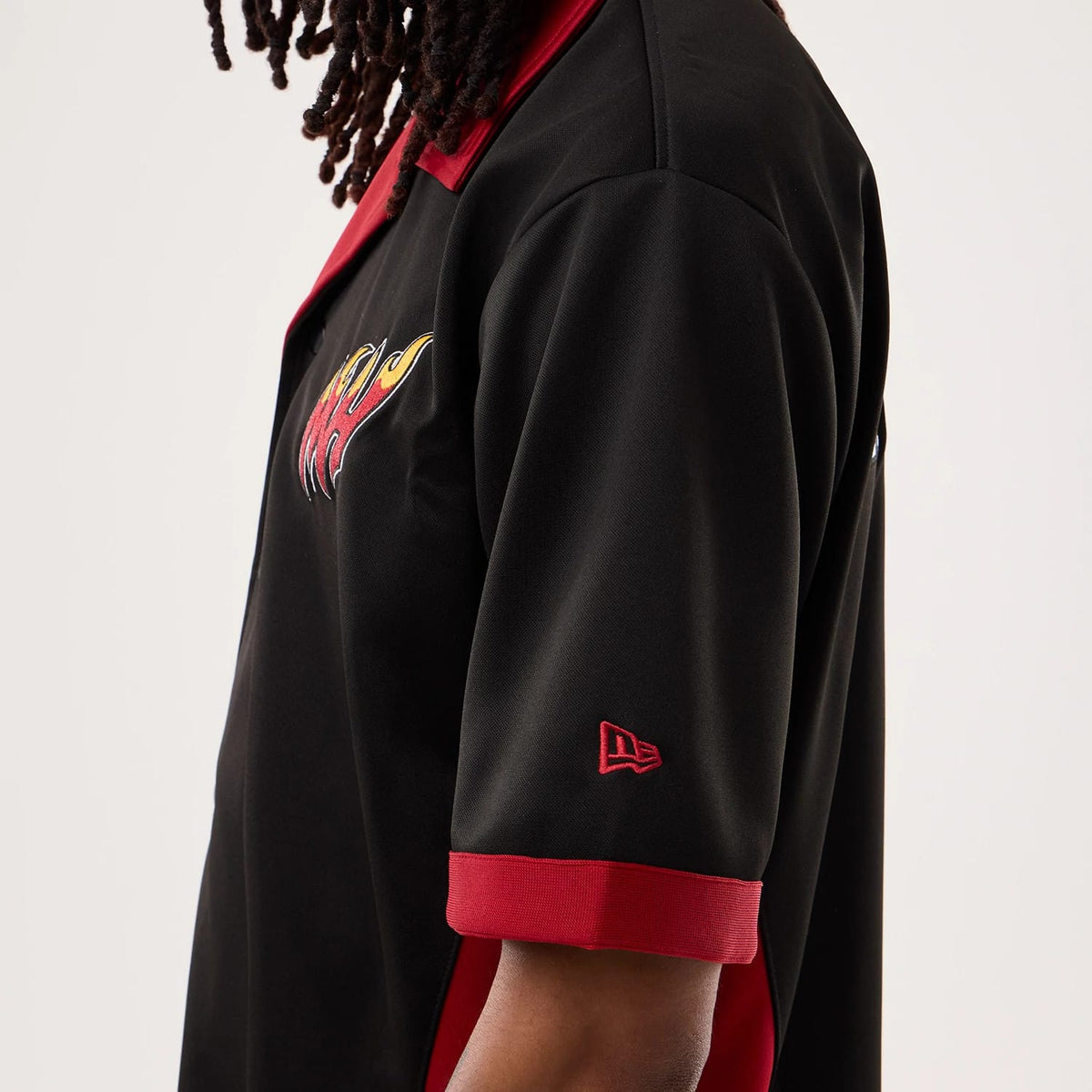 New Era Miami Heat NBA Hardwood Classic Revere Black Short Sleeve Shirt, side view on a model with a red and yellow flame logo embroidered on the chest, red New Era flag logo on the sleeve, and contrasting red collar and sleeve cuffs.