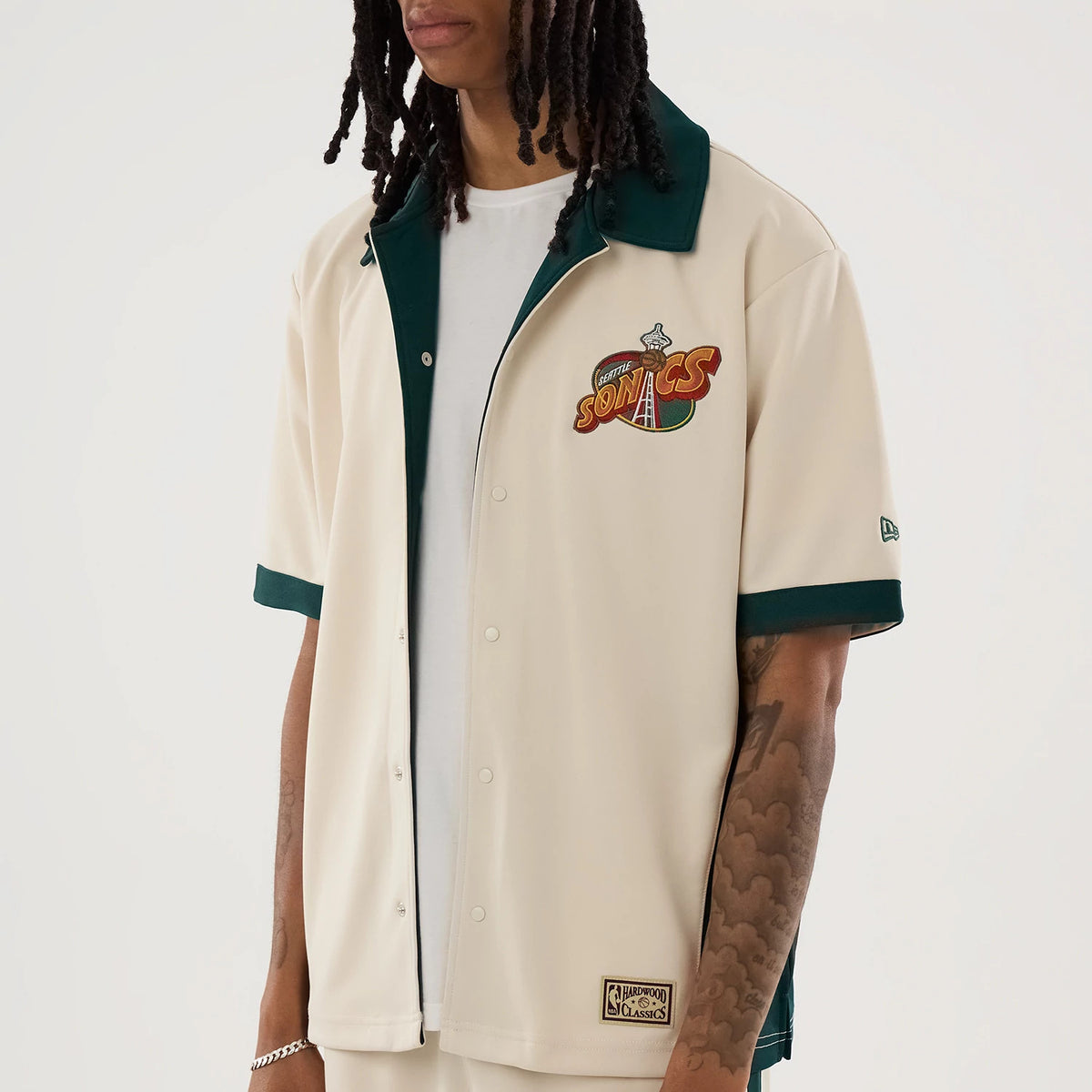 New Era Supersonics NBA Hardwood Classic Revere Beige Short Sleeve Shirt, front view on a model with a white tee underneath, featuring a colourful embroidered Supersonics logo on the left chest, dark green collar.