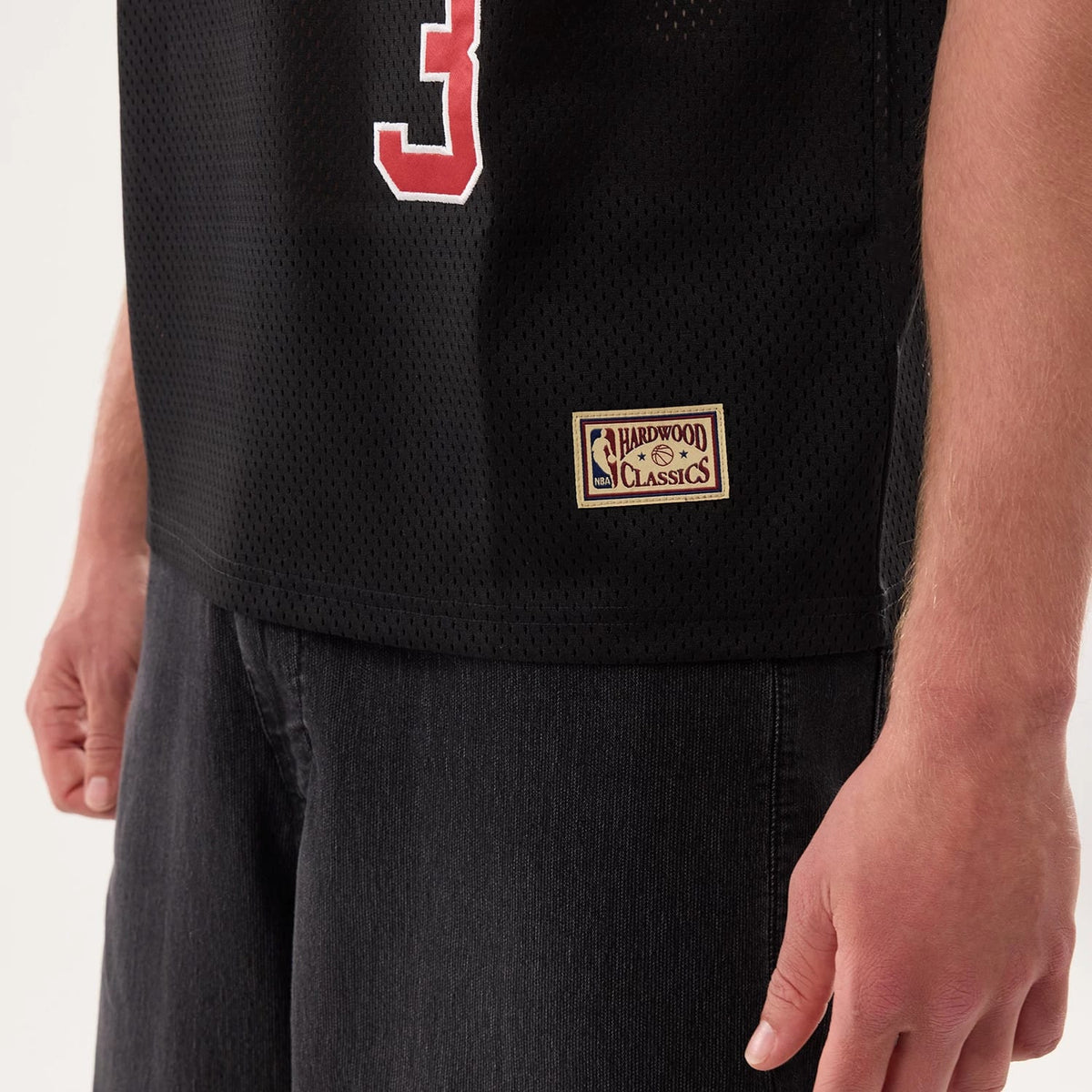 New Era Philadelphia 76ers NBA Hardwood Classic Mesh Oversized Black T-Shirt, side view showing the lower portion with a beige embroidered Hardwood Classics patch on the lower hem, the mesh black fabric texture, and a red.