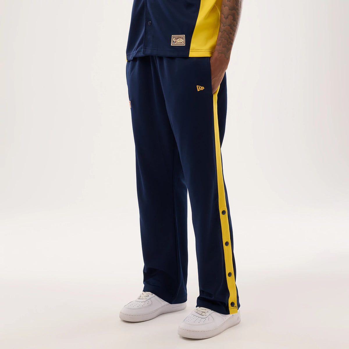 New Era Warriors NBA Hardwood Classic Straight Dark Blue Straight Leg Joggers, on-model view with a relaxed fit, featuring a contrasting yellow side stripe with black button and an embroidered New Era flag logo on the left thigh.