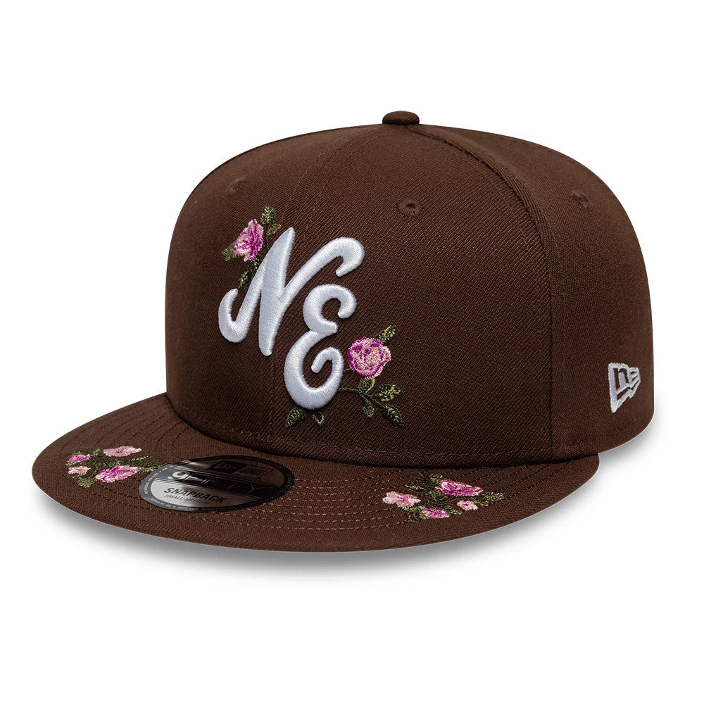 New Era Floral Dark Brown 9FIFTY Snapback Adjustable Cap, three-quarter view showing the raised white NE logo with pink floral embroidery on the front panel, matching floral designs on the visor, and the New Era flag logo on the left side.