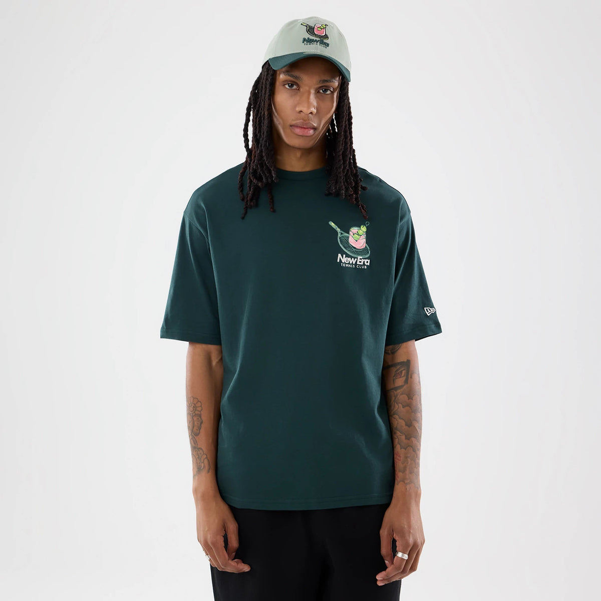 New Era Tennis Graphic Oversized Dark Green T-Shirt, front view on-model showing a large tennis-themed graphic and New Era logo embroidered on the left chest, with a New Era flag embroidered on the left sleeve.