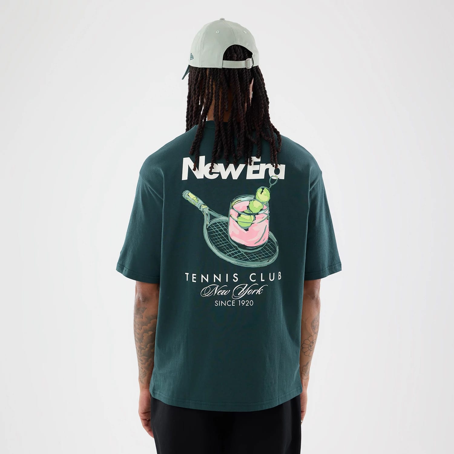 The model is wearing this New Era Tennis Graphic Oversized T-Shirt in dark green. 2