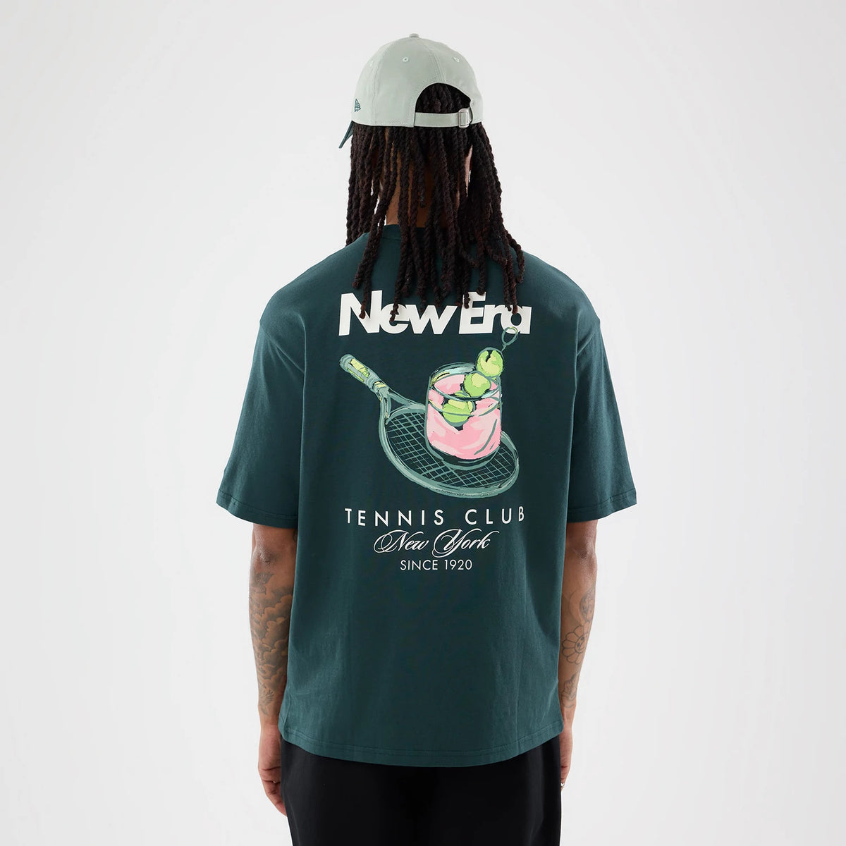 New Era Tennis Graphic Oversized Dark Green T-Shirt, back view showing a large white printed New Era logo across the upper back, a tennis racquet and tennis balls graphic below, and Tennis Club New York Since 1920 text at the bottom.