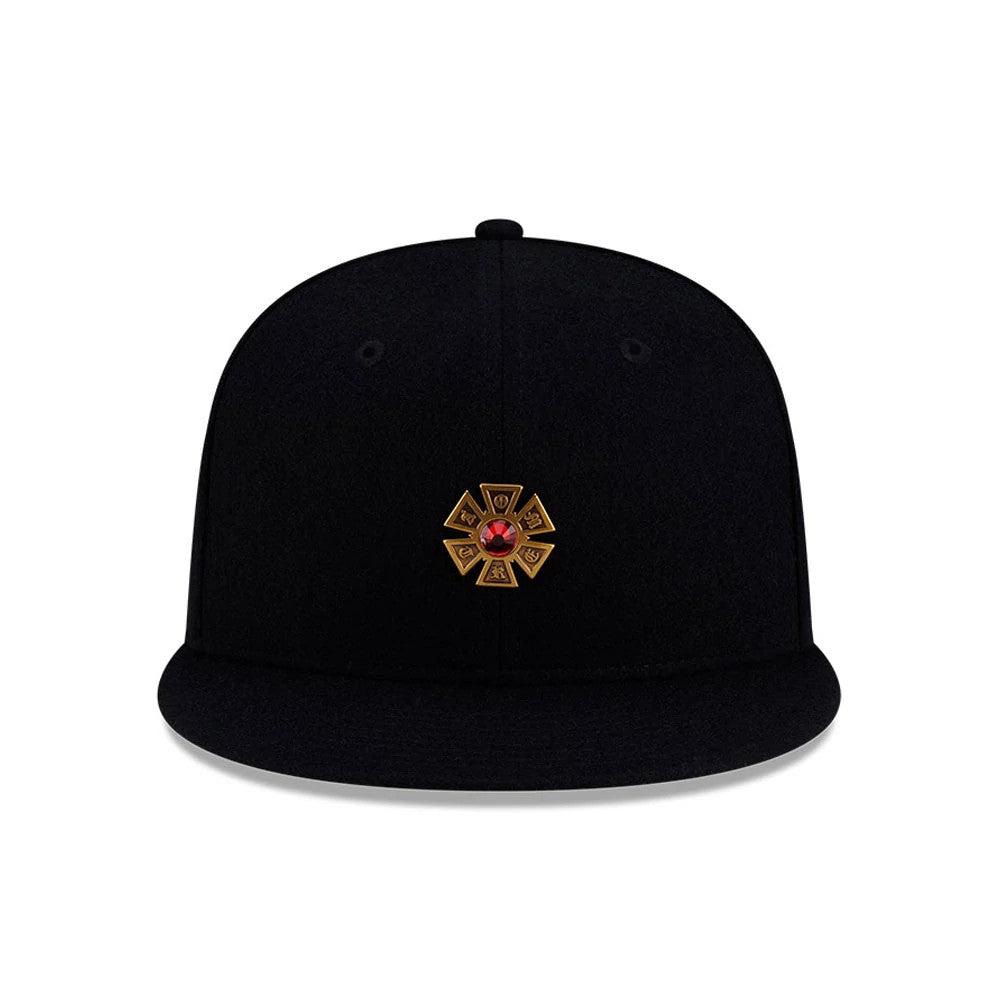 New Era X Omerta Balvin Black 59FIFTY Fitted Cap, front view showing a gold embroidered geometric logo with a red gem at the centre of the black structured crown, flat black visor, and black eyelets and top button.