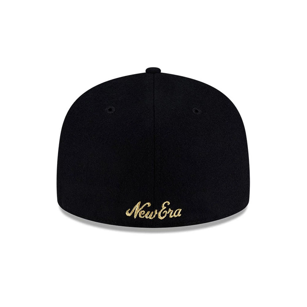 New Era X Omerta Balvin Black 59FIFTY Fitted Cap, side view showing gold embroidered smiley face and abstract design on the structured black crown, with a curved black visor and New Era flag logo on the left side.