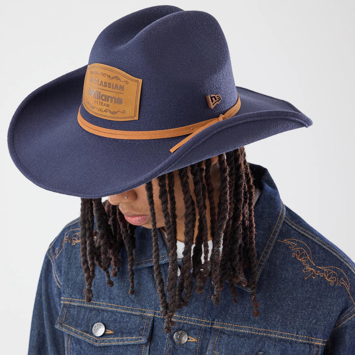 New Era Williams Austin Race Special Navy Wide Brim Fedora Cowboy Hat, on-model view with a tan band accentuating the navy crown, a tan patch featuring the Williams logo on the front panel, and the New Era flag logo on the side.