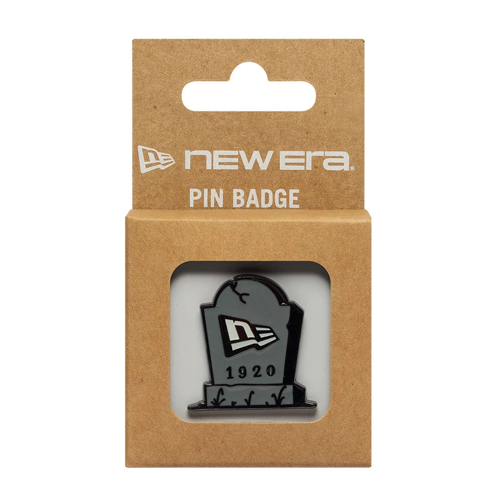 New Era Halloween Grave Grey Pin Badge, front view showing a grey tombstone design with an embossed New Era logo at the centre and 1920 underneath, enclosed in a square, brown cardboard packaging with New Era branding at the top.