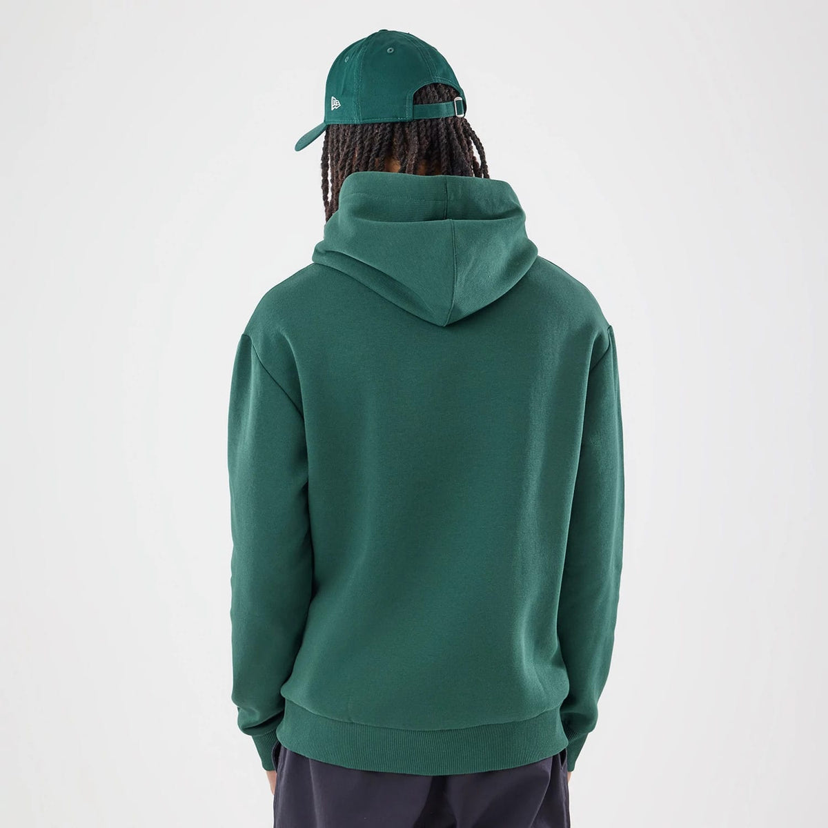 New Era Carlos Sainz Team Fifty5 Smooth Dark Green Oversized Pullover Hoodie, back view on a model featuring a generously sized hood and ribbed hem, styled with a matching dark green cap showcasing an embroidered New Era logo on the side.