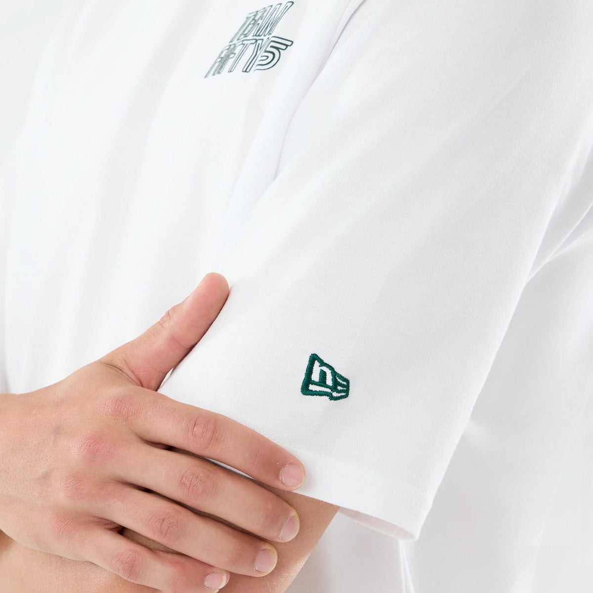 New Era Carlos Sainz Team Fifty5 Mexico White Oversized T-Shirt, side view showing a close-up of the sleeve with an embroidered green New Era logo near the hem, and the Team Fifty5 lettering on the chest against the white fabric.