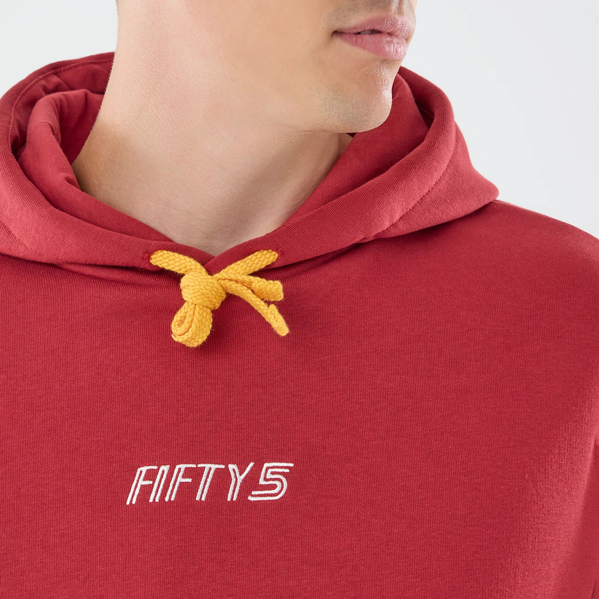 New Era Carlos Sainz Team Fifty5 Madrid Dark Red Oversized Pullover Hoodie, front view on a model highlighting the embroidered Fifty5 logo centred on the chest, the hood with a bright yellow drawstring, and the dark red fabric.