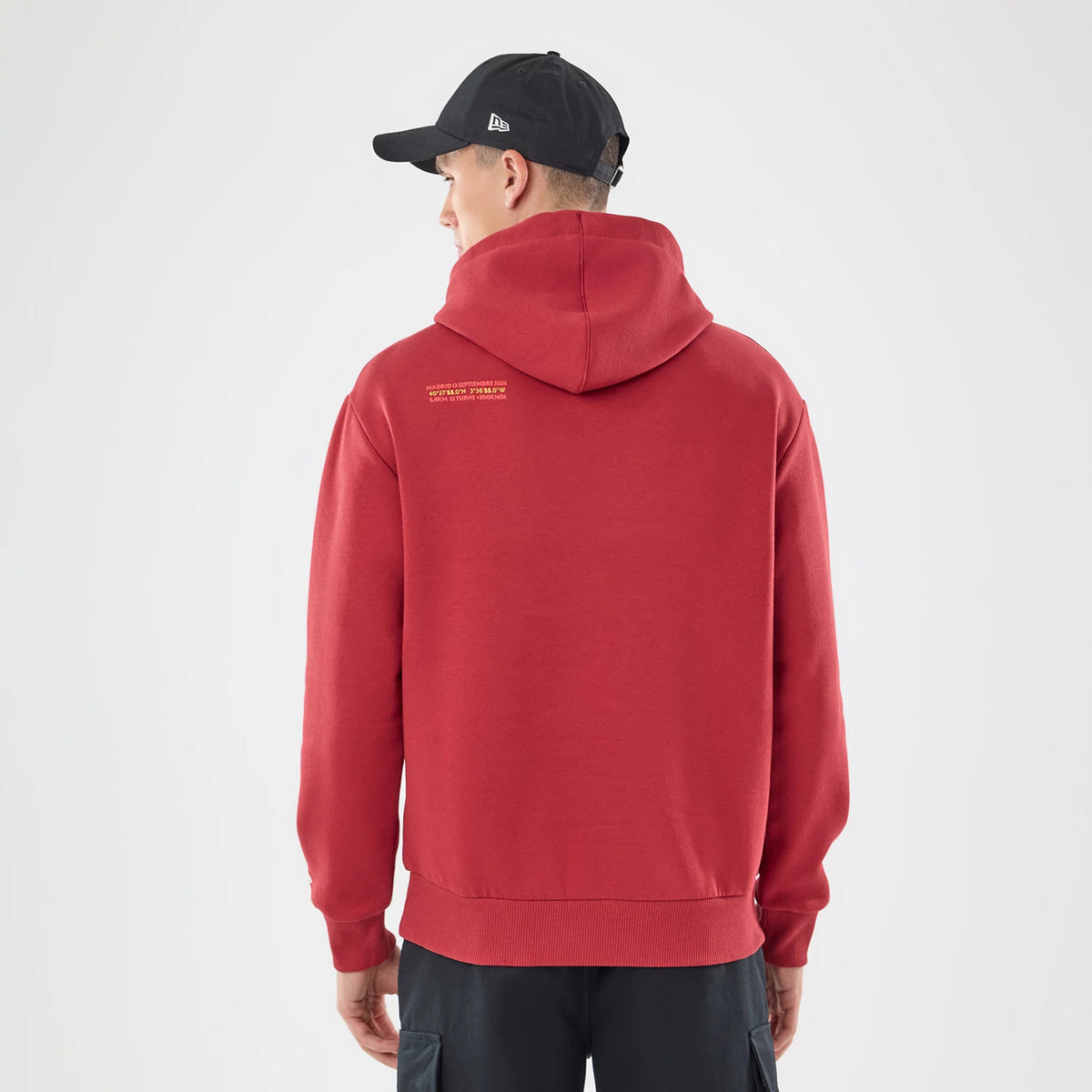 New Era Carlos Sainz Team Fifty5 Madrid Dark Red Oversized Pullover Hoodie, back view on a model styled with a black cap, featuring small yellow printed text across the upper back and a generously sized hood resting at the neck.