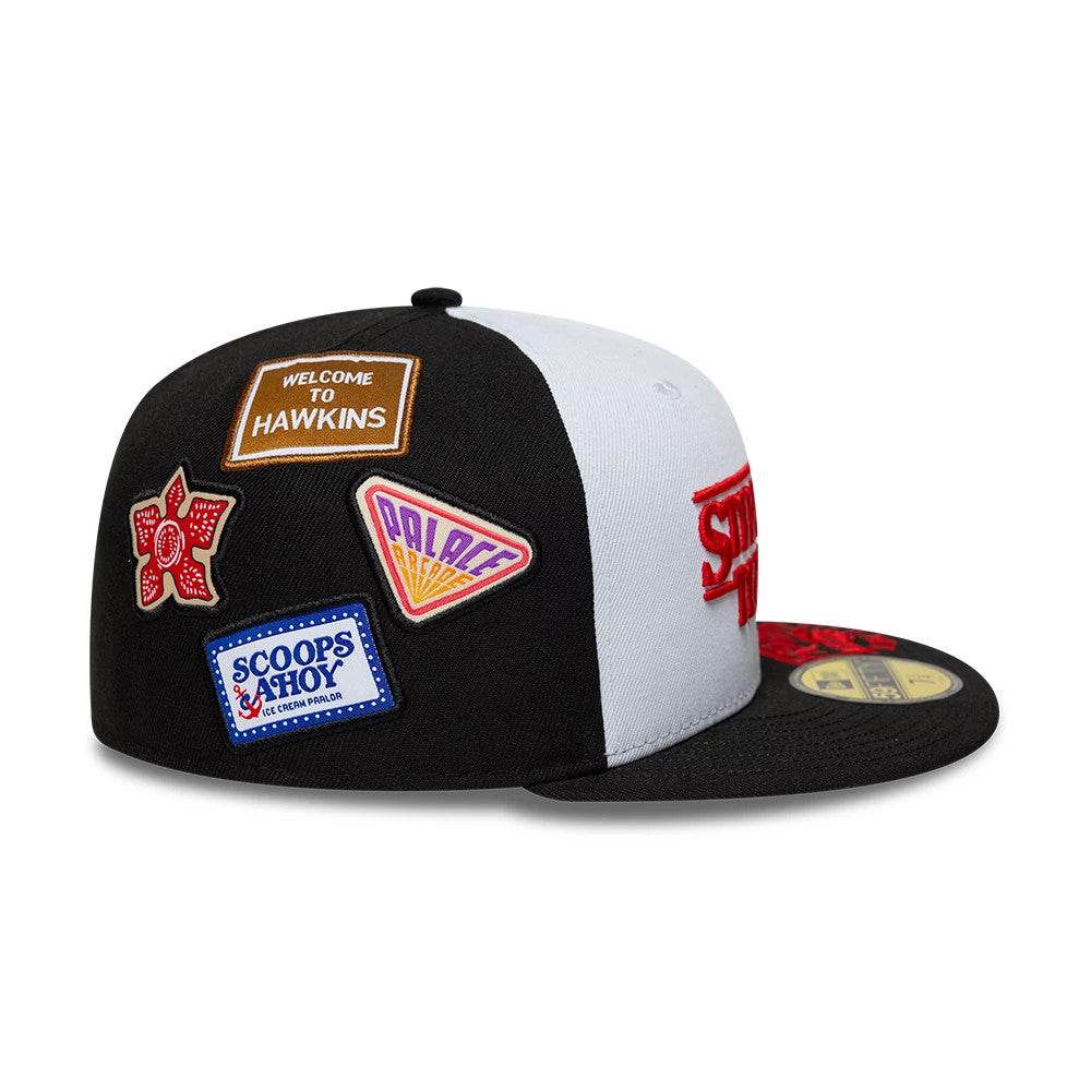 Netflix Stranger Things 10 Years Black New Era 59FIFTY Fitted Cap, side view showing multiple embroidered patches including a red flower, Welcome to Hawkins, Palace Arcade, and Scoops Ahoy, on a structured black.