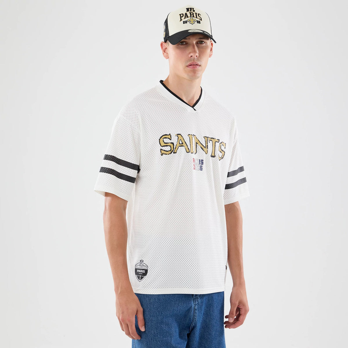 New Era New Orleans Saints NFL International Games 2026 Graphic White Mesh Jersey, front view on a model with the black 'SAINTS' text in distressed gold embroidery across the chest, double black stripes on each sleeve.