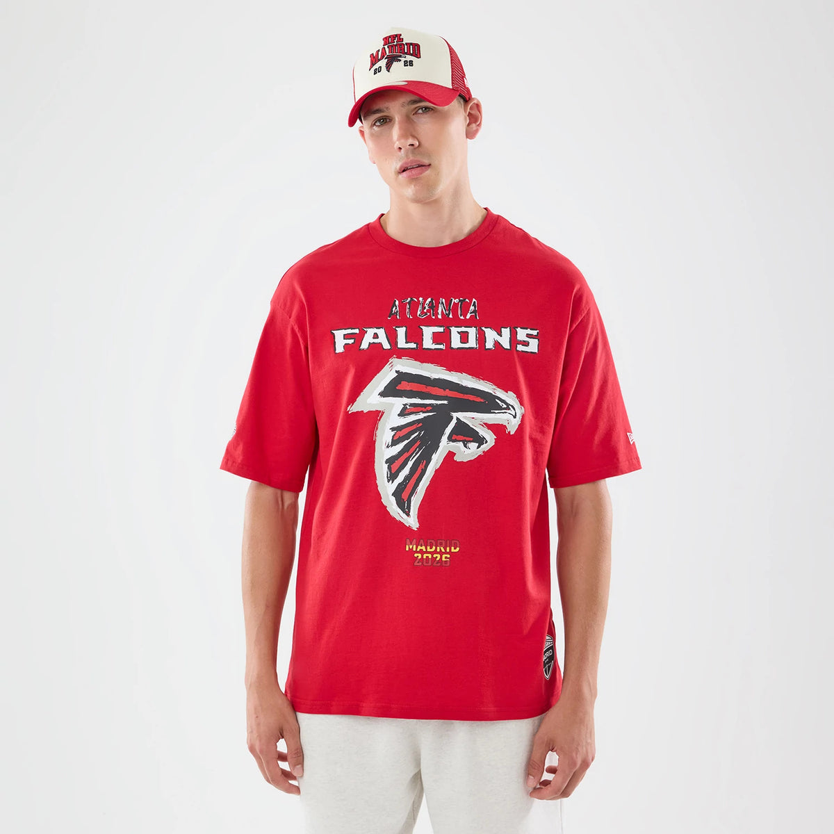 New Era Atlanta Falcons NFL Graphic Slogan Red Oversized T-Shirt, front view showing a large Falcons logo centred on the chest, ATLANTA FALCONS text above it in distressed white, and MADRID 2023 below, worn by a model with a matching red.