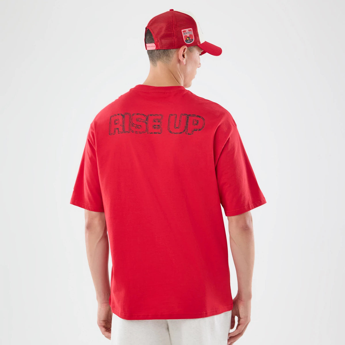 New Era Atlanta Falcons NFL Graphic Slogan Red Oversized T-Shirt, back view on a model wearing a red cap, featuring RISE UP lettering across the upper back, highlighting the red colour and loose fit of the oversized tee.