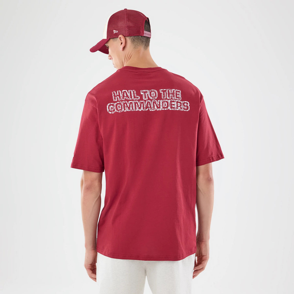New Era Washington Commanders NFL Graphic Slogan Dark Red Oversized T-Shirt, back view showing the Hail To The Commanders slogan prominently printed in white across the upper back, worn by a model with a matching cap, highlighting the oversized fit.