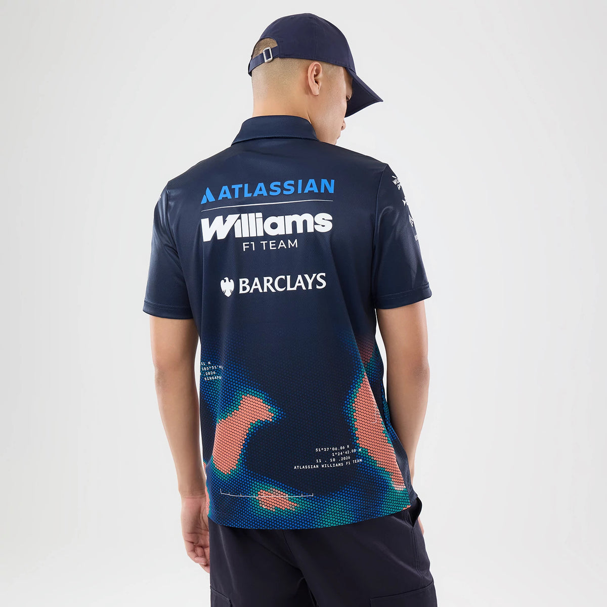 New Era Williams Singapore Navy Tech Polo T-Shirt, back view on a model wearing a navy cap, featuring white Williams F1 Team lettering across the upper back, Atlassian and Barclays logos above and below, and a blue and coral abstract pattern.