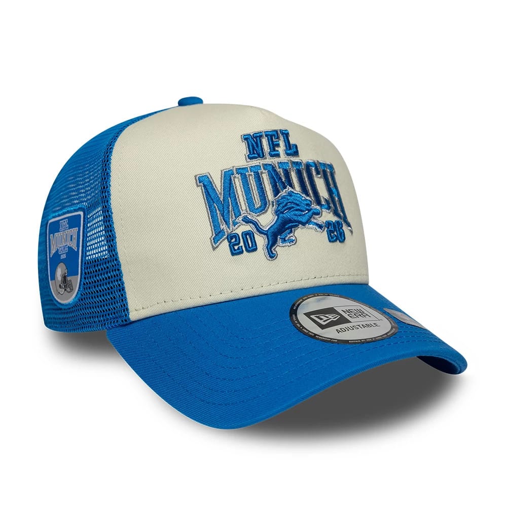 Lions NFL International Games 2026 Munich Blue New Era 9FORTY A-Frame Trucker Adjustable Cap, three-quarter view showing blue embroidered NFL Munich 2026 logo on the front panels, blue visor with New Era 9FORTY size sticker.