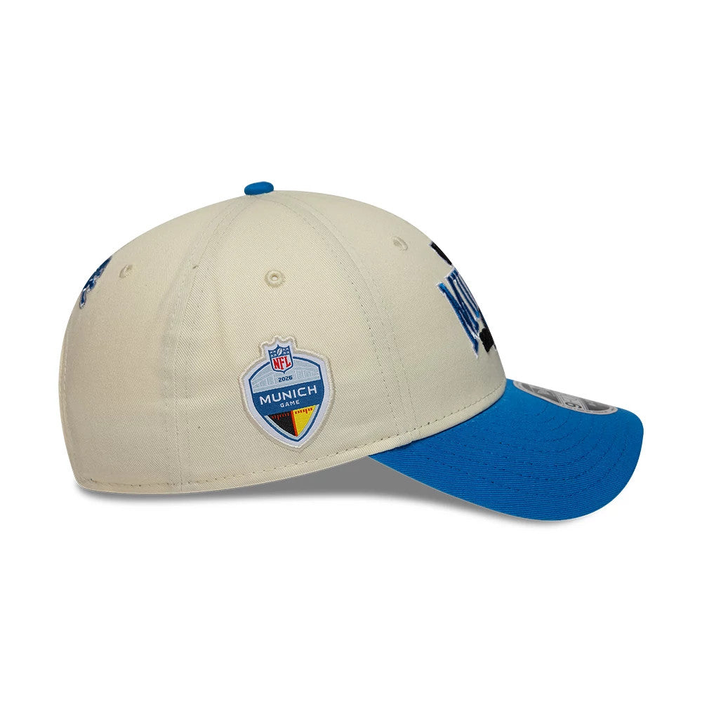 Lions NFL International Games 2026 Munich White & Blue New Era 9FORTY M-Crown Adjustable Cap, side view showing the embroidered Munich 2026 shield on the cream crown, an embroidered Lions logo on the front panel.