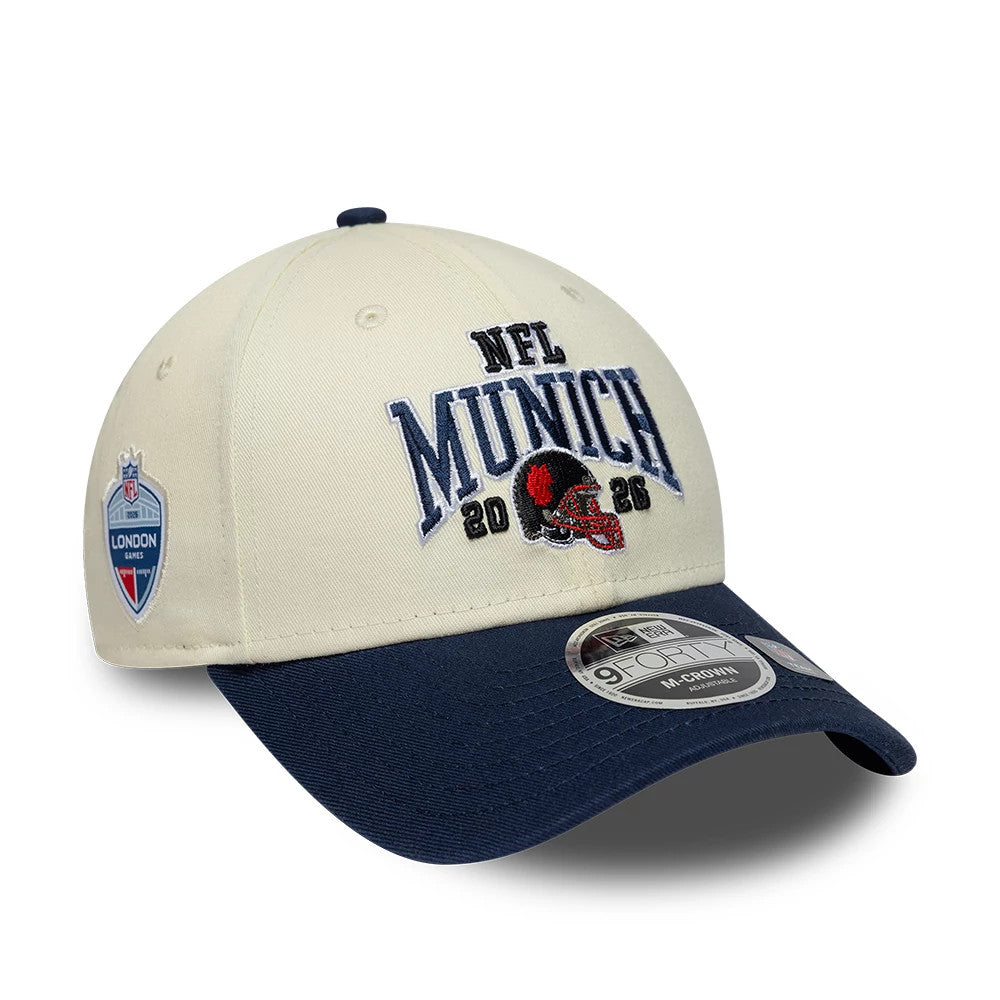 Patriots NFL International Games 2026 Munich White & Dark Blue New Era 9FORTY M-Crown Adjustable Cap, three-quarter view showing dark blue embroidered NFL Munich 2026 text and helmet on the front panel, dark blue curved visor.