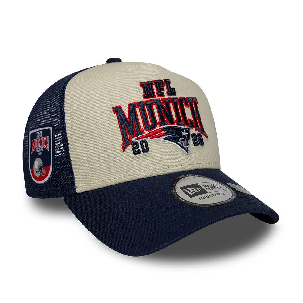 Patriots NFL International Games 2026 Munich Dark Blue New Era 9FORTY A-Frame Trucker Adjustable Cap, front view showing raised red and blue embroidered NFL Munich 2026 logo on tan front panel, dark blue curved visor with 9FORTY size sticker.