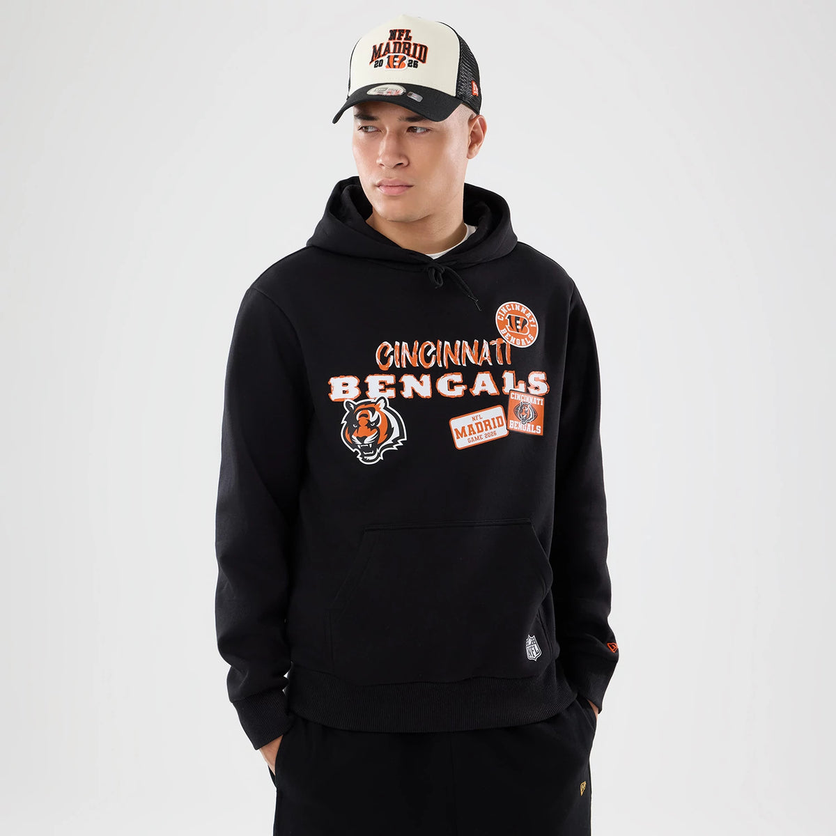 New Era Cincinnati Bengals NFL International Games 2026 Black Pullover Hoodie, front view on a model wearing a matching cap, featuring embroidered Cincinnati Bengals lettering, a large tiger logo on the left chest, and NFL Madrid.