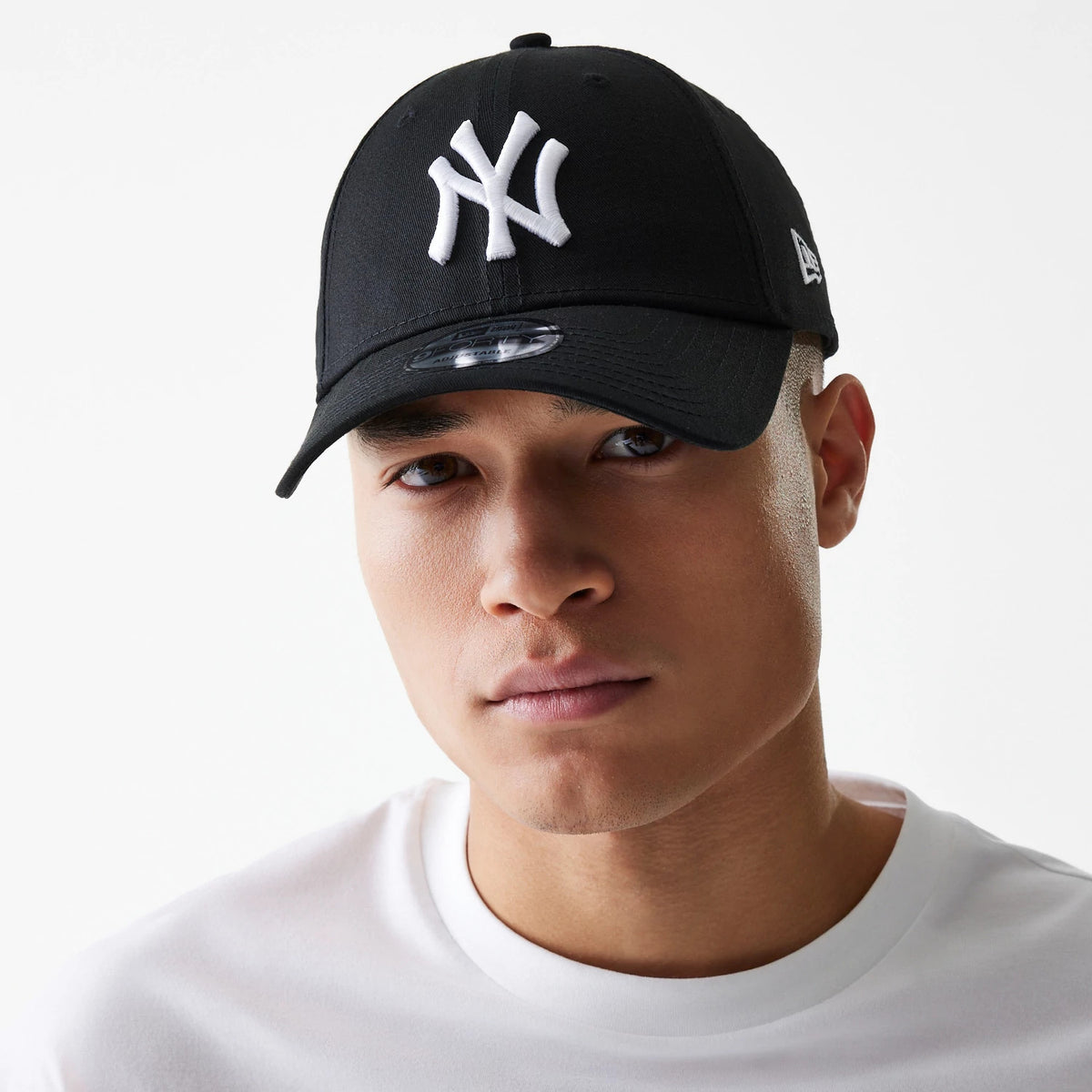 New York Yankees Essential Black New Era 9FORTY Cap, on-model front view with raised white NY logo on the front panel and New Era flag logo on the left side, paired with a white T-shirt.