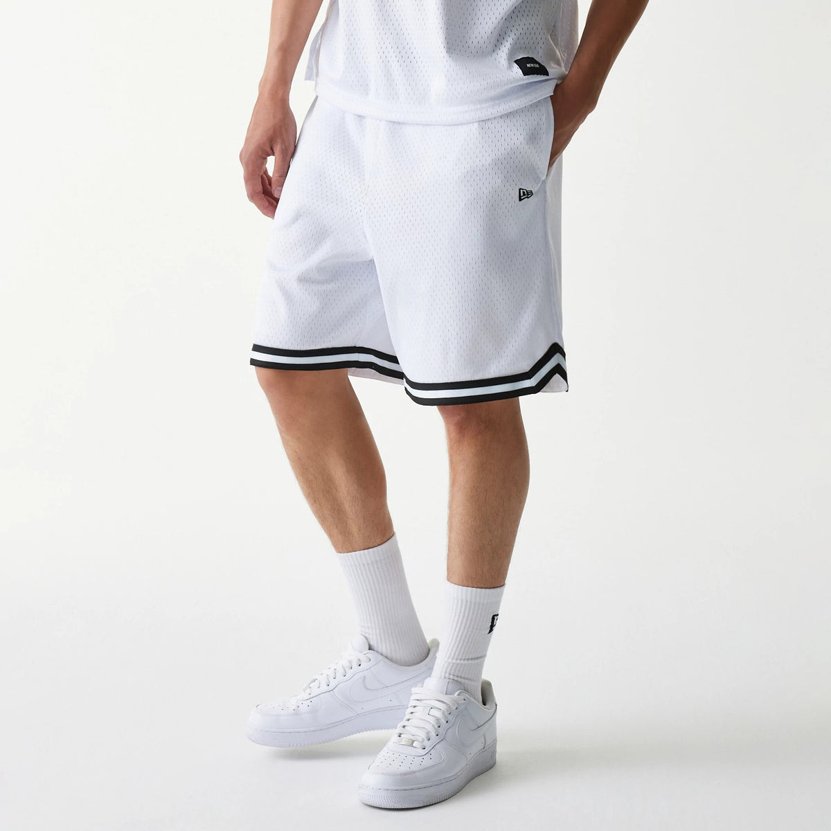 New Era Japan Mesh White Shorts, on-model view showing the white shorts with black trim at the hem and a raised New Era logo on the left leg, complemented by a matching white top and trainers.